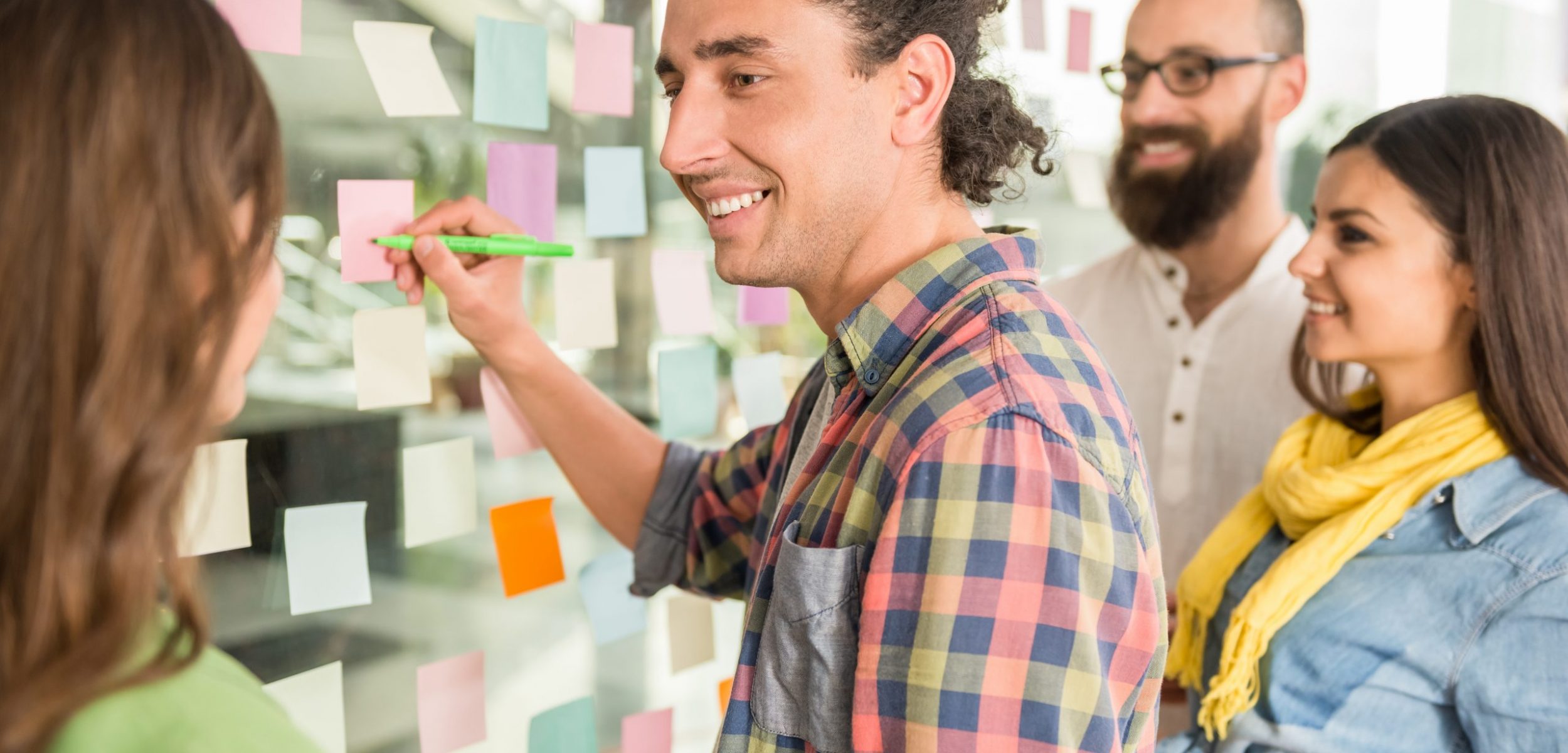 Creative team working on new project with many sticky notes on window.